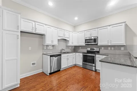 a kitchen with stainless steel appliances granite countertop white cabinets a sink a stove a refrigerator and microwave with wooden floor