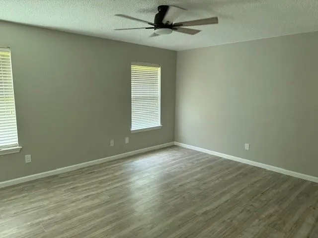 an empty room with wooden floor fan and windows