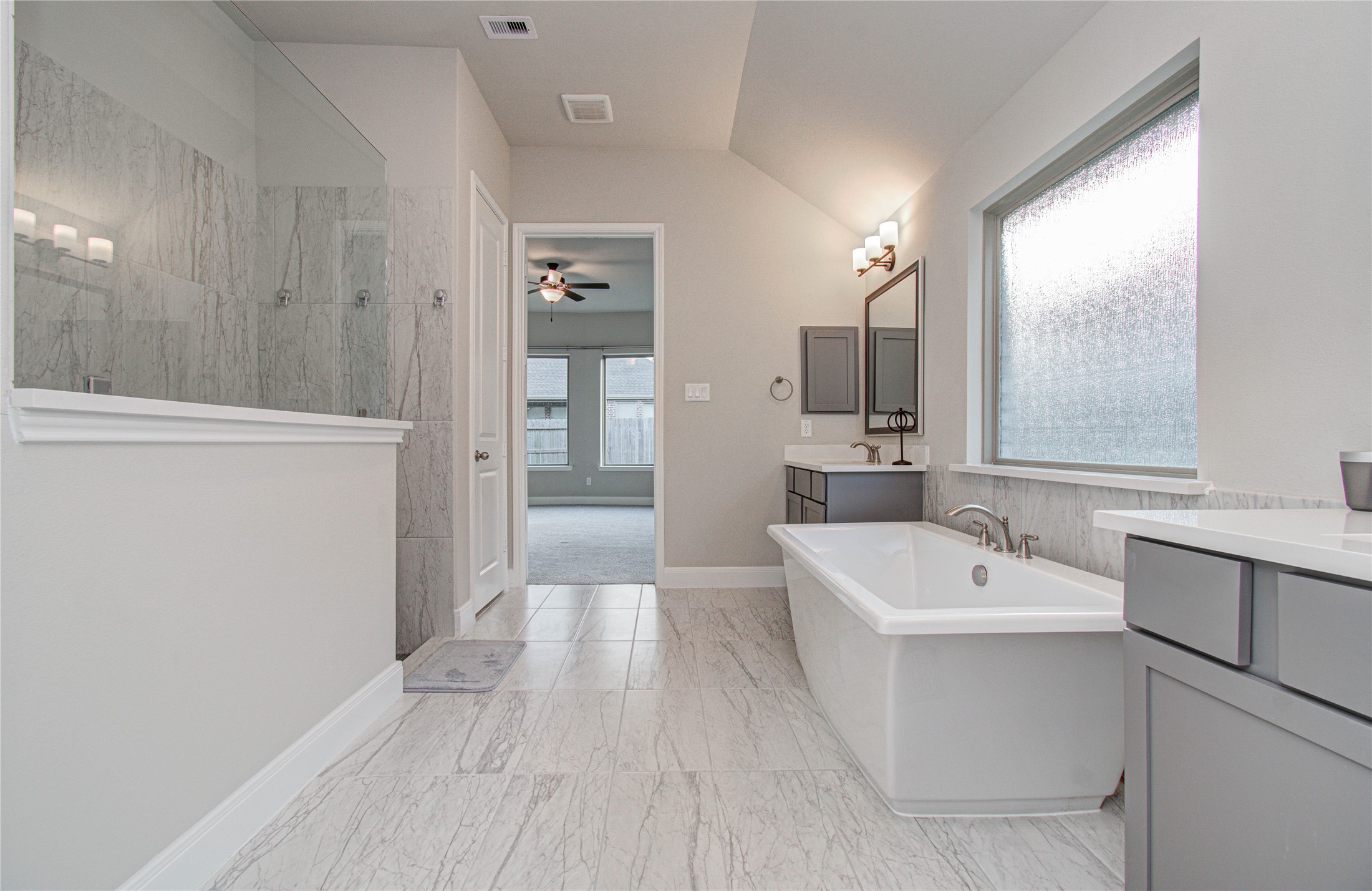 17344 Grand Canyon Road Conroe, TX 77302 - Photo 26 of 49 This spacious bathroom features a large soaking tub, a glass-enclosed shower, and modern fixtures. It has elegant marble flooring and countertops, with ample natural light from a frosted window.