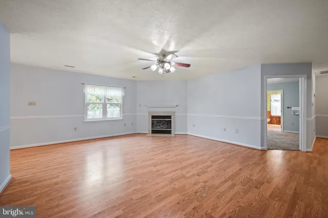 an empty room with wooden floor a chandelier fan and windows