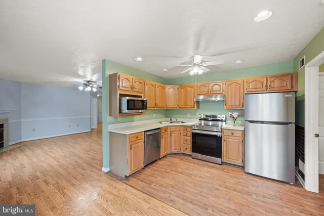 a kitchen with stainless steel appliances granite countertop a refrigerator a stove top oven a sink and dishwasher with wooden floor