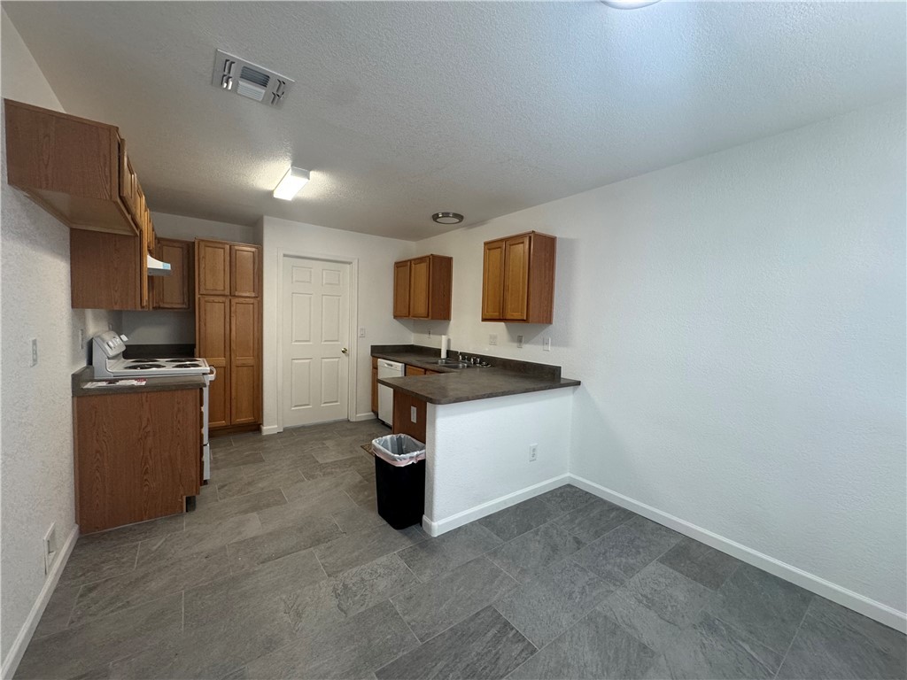 3442 Sunriver Road Bullhead City, AZ 86429 - Photo 3 of 3 Kitchen featuring dark countertops, brown cabinetry, range with electric cooktop, a peninsula, and a textured ceiling