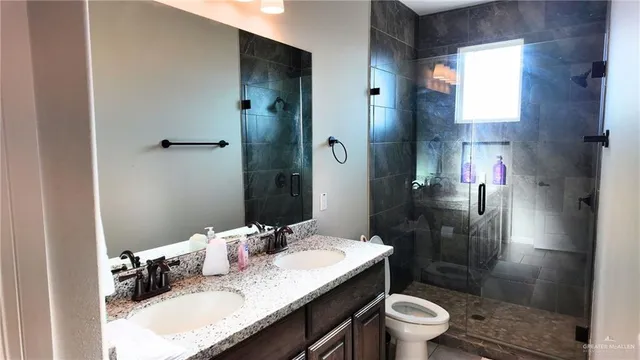 a bathroom with a granite countertop sink a toilet a mirror and shower