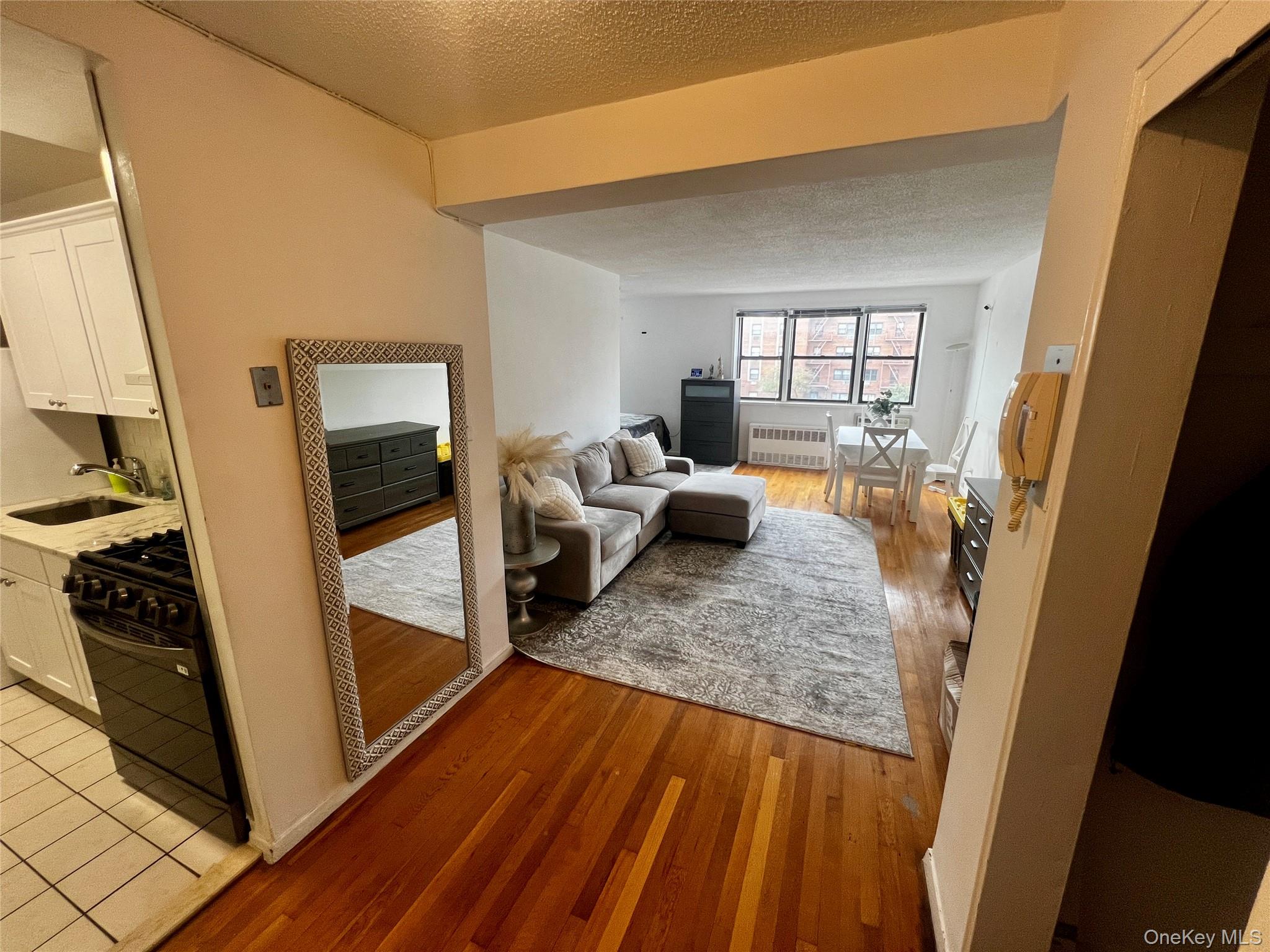 Living room with a textured ceiling, light wood-style floors, and radiator heating unit
