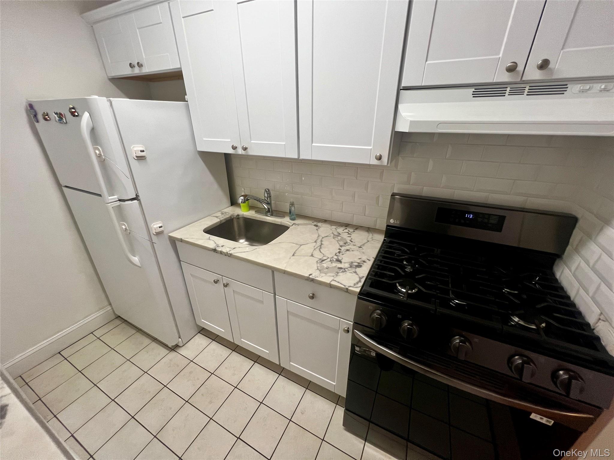 84-29 155th Avenue, Unit 2H Queens, NY 11414 - Photo 10 of 38 Kitchen with black gas range, white cabinets, freestanding refrigerator, and under cabinet range hood