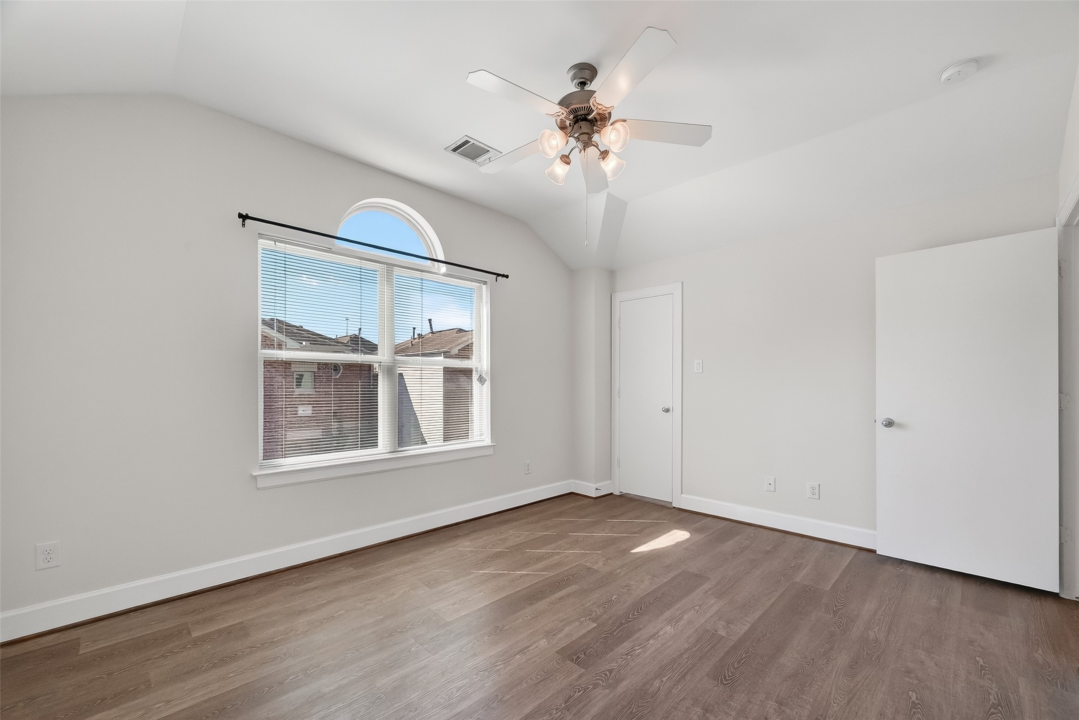 5951 S Loop East, Unit 47 Houston, TX 77033 - Photo 27 of 37 Bright room with natural light, featuring a large window with blinds and an arched design above. The space has a ceiling fan, light-colored walls, and wood flooring, providing a modern and airy feel.