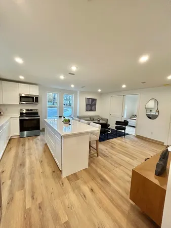 a large white kitchen with stainless steel appliances kitchen island a stove a refrigerator a oven and a sink with large countertops