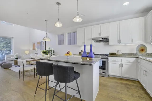 a kitchen with stainless steel appliances granite countertop a sink dishwasher a stove a refrigerator a microwave oven with white cabinets and wooden floor