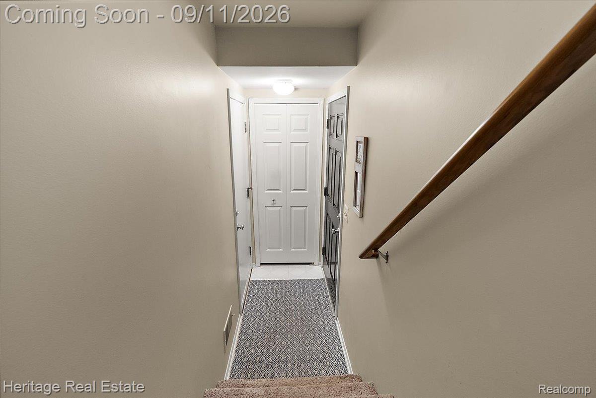 3088 High Pointe Ridge Road Lake Orion, MI 48359 - Photo 23 of 31 Hallway featuring a brown wood handrail, light beige walls, and a patterned floor mat