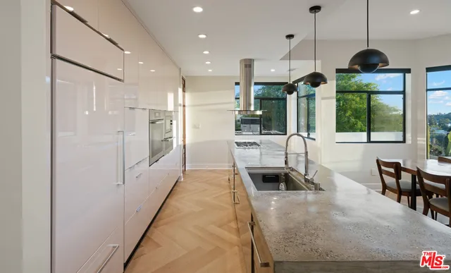 a kitchen with stainless steel appliances granite countertop a refrigerator a oven a sink a dining table and chairs with wooden floor