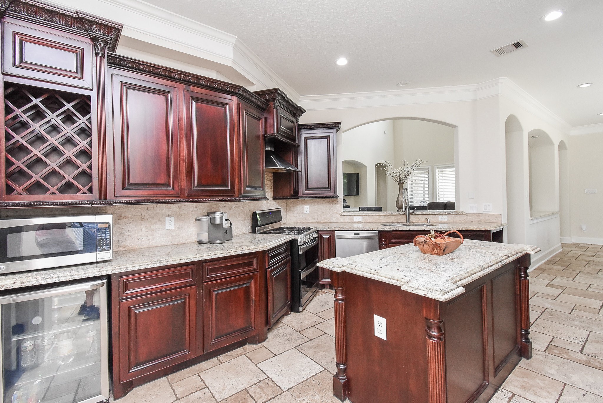 633 Crenshaw Road Houston, TX 77504 - Photo 12 of 46 This spacious kitchen features rich wooden cabinetry with a built-in wine rack, modern stainless steel appliances, and granite countertops. The open layout connects seamlessly to the living area, highlighted by a central island perfect for meal prep or casual dining. Recessed lighting and neutral tile flooring add a bright and elegant touch.