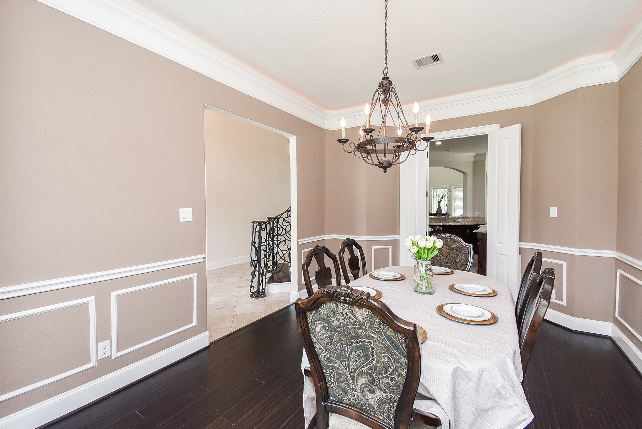 633 Crenshaw Road Houston, TX 77504 - Photo 14 of 46 This dining room features elegant wainscoting, a classic chandelier, and dark hardwood floors. It has a traditional feel with ample space for a large dining table, and it opens to a hallway with decorative iron railing and tiled floors.