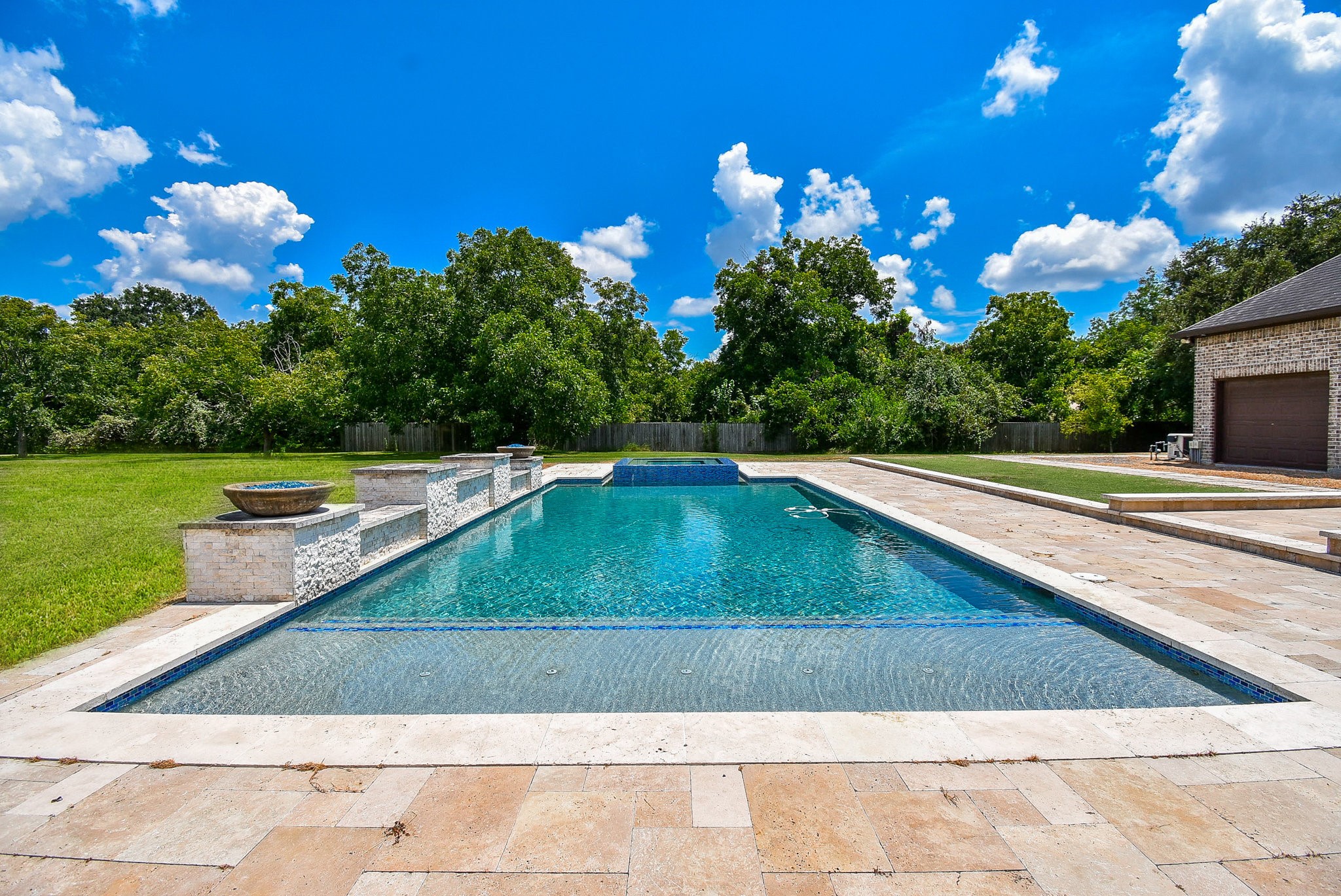 633 Crenshaw Road Houston, TX 77504 - Photo 21 of 46 This photo showcases a luxurious backyard with a spacious rectangular pool, surrounded by a stone patio. The area is bordered by lush greenery and has a serene, private feel, ideal for relaxation and outdoor activities.