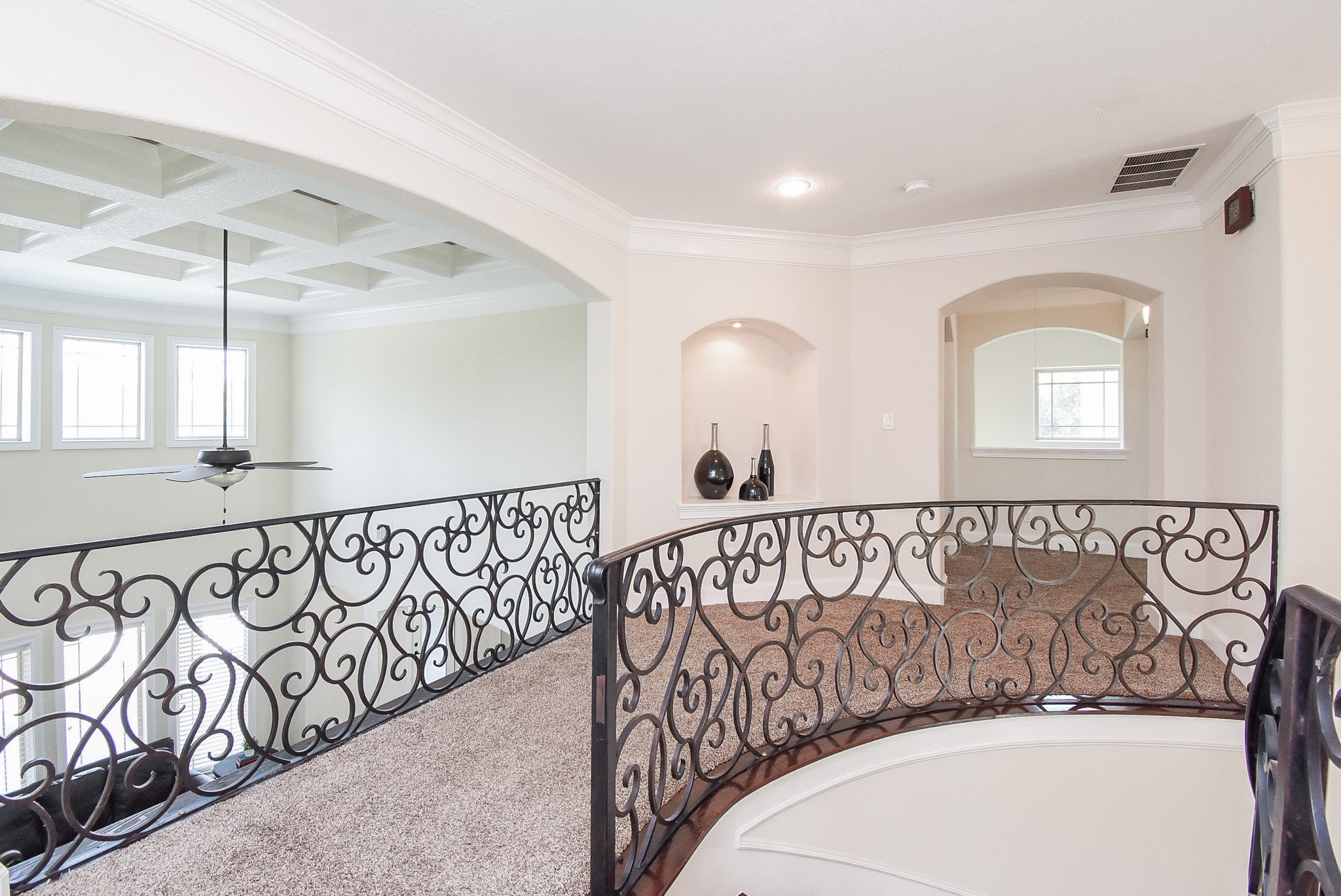 633 Crenshaw Road Houston, TX 77504 - Photo 22 of 46 This photo showcases a spacious upper landing with elegant wrought iron railings, arched doorways, and a coffered ceiling. Natural light pours in through multiple windows, highlighting the open and airy feel.