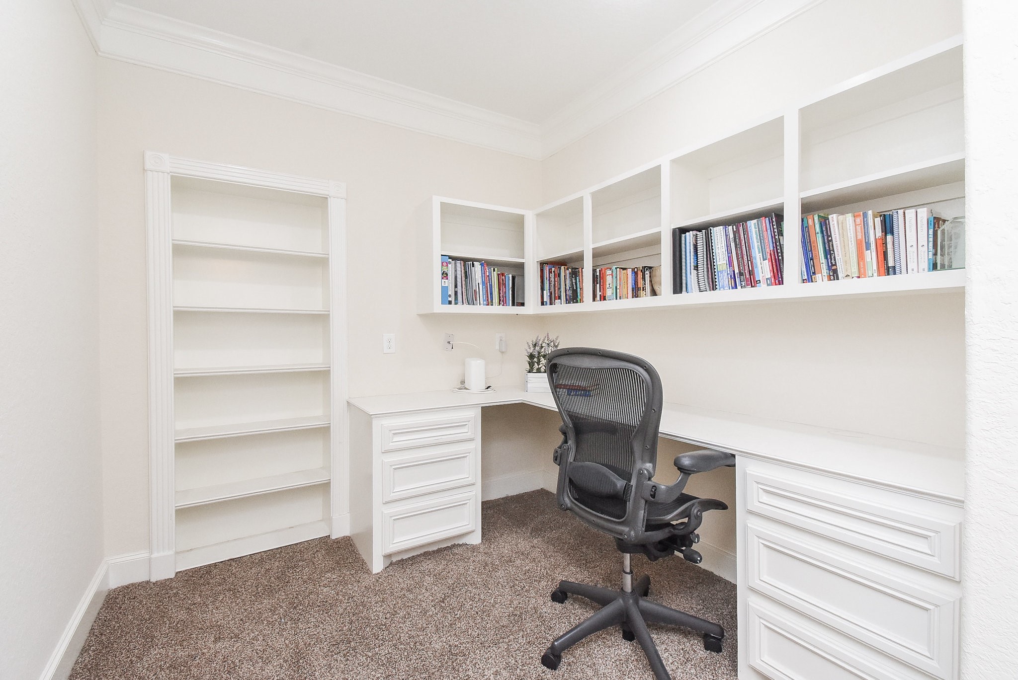 633 Crenshaw Road Houston, TX 77504 - Photo 34 of 46 This photo showcases a bright home office with built-in shelving, a spacious desk, and a comfortable office chair. The room is carpeted and offers ample storage space, ideal for a productive workspace.