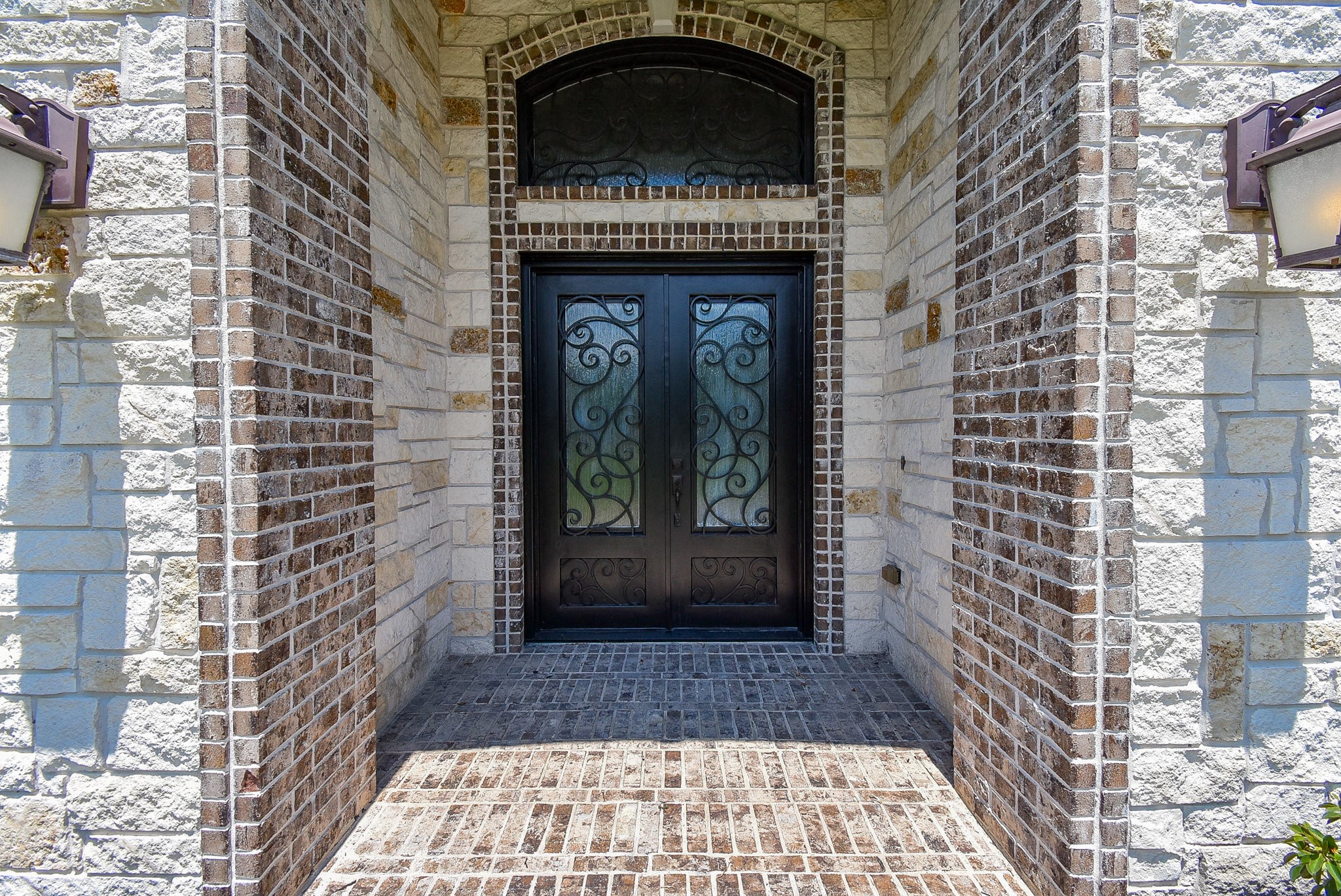 633 Crenshaw Road Houston, TX 77504 - Photo 4 of 46 This photo showcases an elegant front entrance with a dark, ornate wrought iron door set within a brick and stone facade, creating a welcoming and sophisticated first impression.