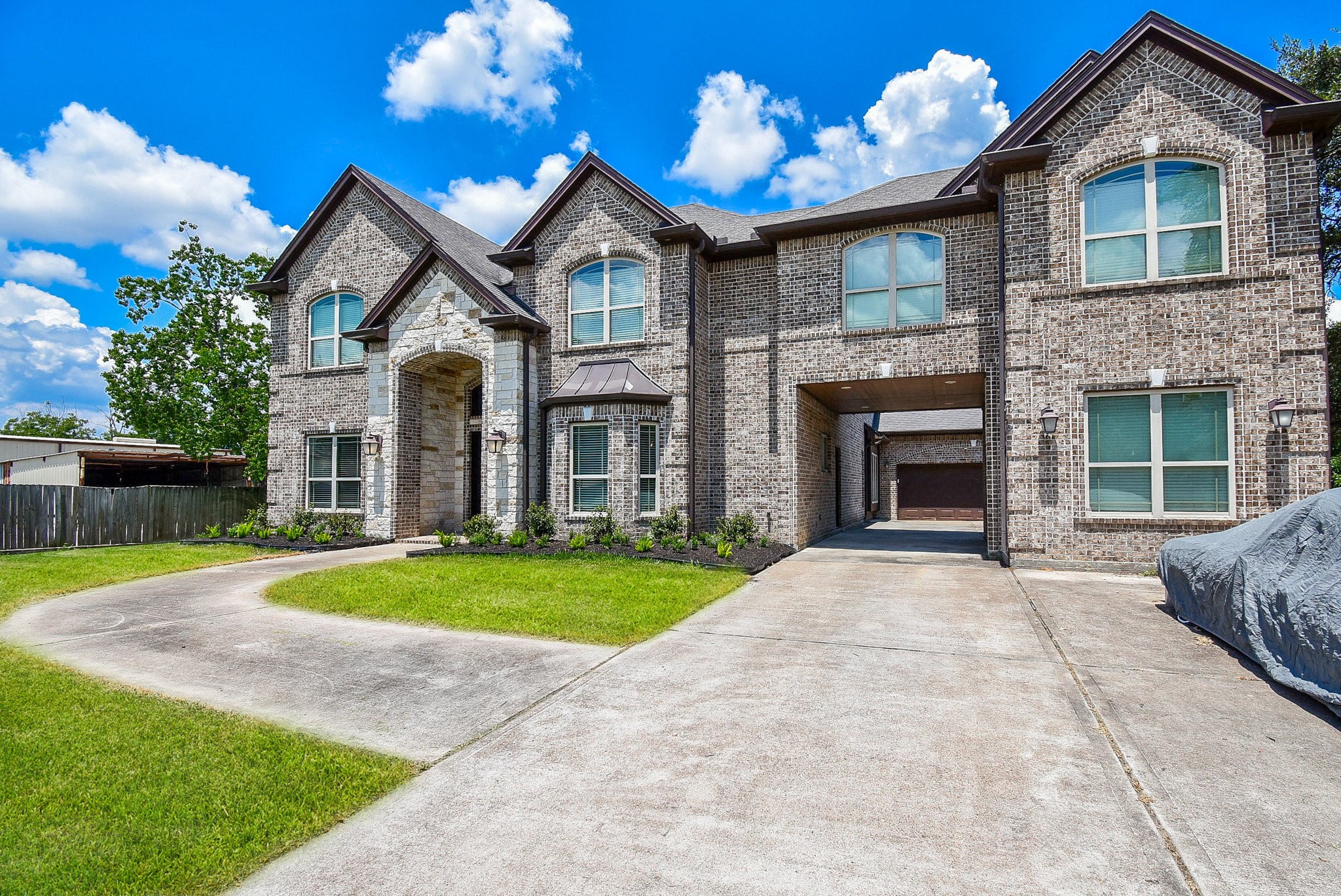 633 Crenshaw Road Houston, TX 77504 - Photo 40 of 46 This photo showcases a large, two-story brick house with a modern design. It features a double-arched entryway, multiple windows, and a spacious driveway leading to a covered archway and garage. The well-maintained lawn and landscaped front add to its curb appeal.