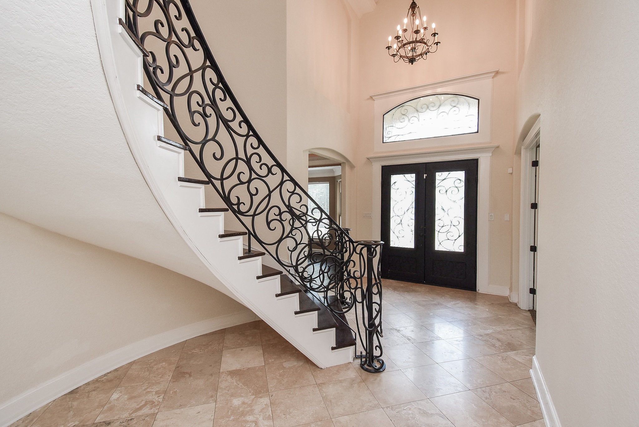 633 Crenshaw Road Houston, TX 77504 - Photo 5 of 46 This elegant entryway features a grand spiral staircase with ornate wrought-iron detailing, a chandelier, and double doors with decorative glass. The space is bright and welcoming, with polished tile flooring and high ceilings.