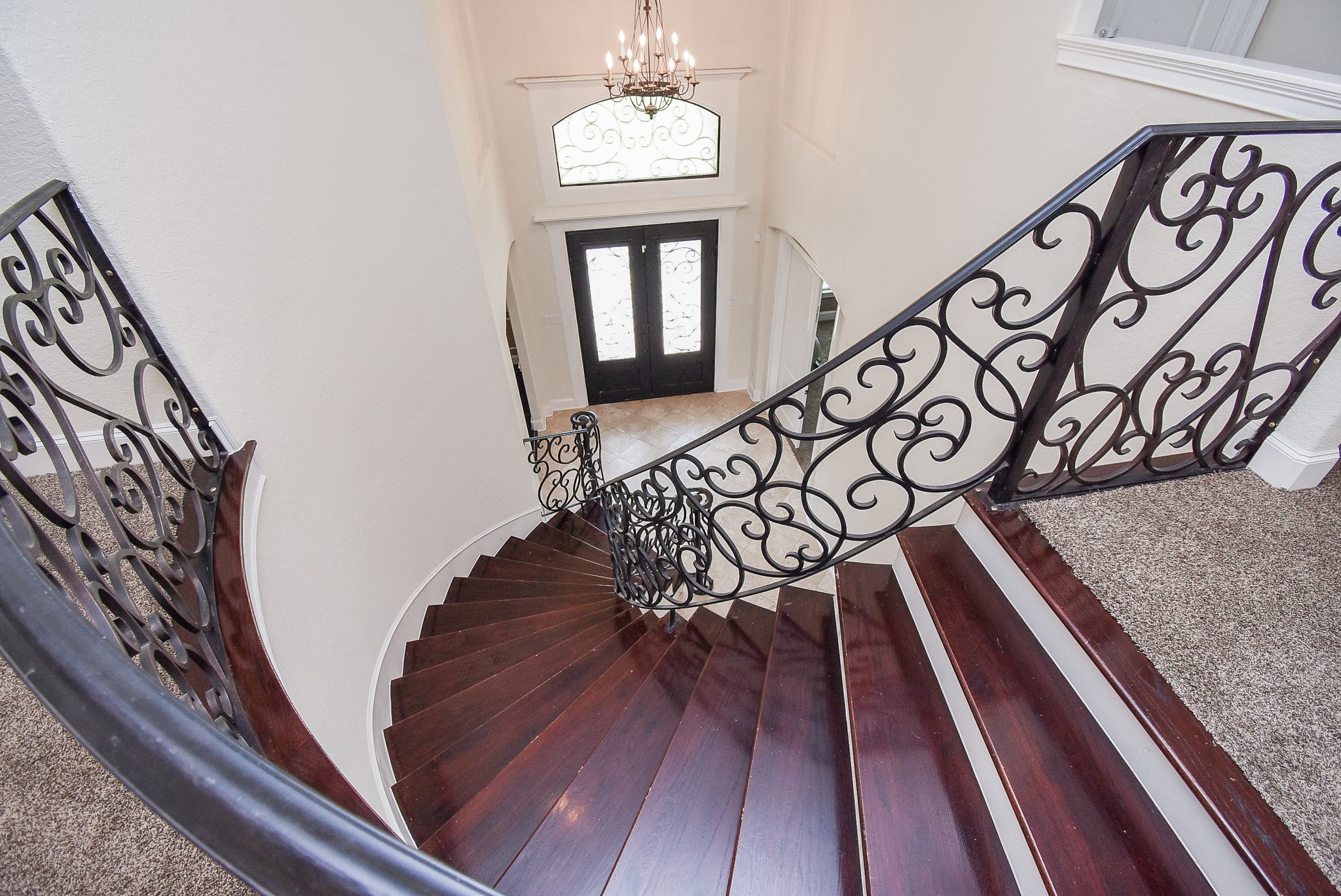 633 Crenshaw Road Houston, TX 77504 - Photo 7 of 46 This elegant home features a grand, curved staircase with dark wood steps and ornate wrought iron railings. The entryway is bright and inviting, highlighted by a chandelier and double doors with decorative glass panels.