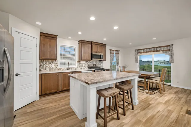 a kitchen with stainless steel appliances kitchen island granite countertop a table chairs sink and cabinets