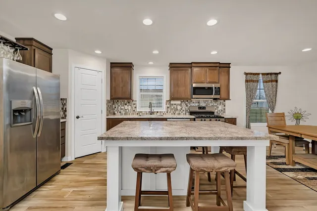 a kitchen with stainless steel appliances granite countertop a table chairs refrigerator and sink