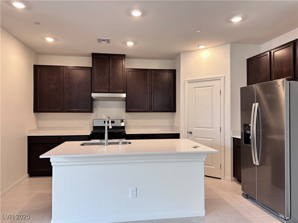 3634 Cameri Avenue Henderson, NV 89044 - Photo 4 of 22 Kitchen with appliances with stainless steel finishes, dark brown cabinetry, a kitchen island with sink, recessed lighting, and light tile patterned flooring