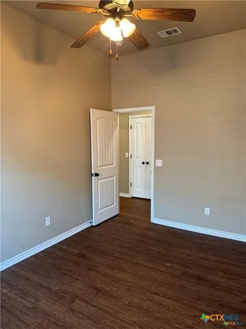 an empty room with wooden floor chandelier fan and windows