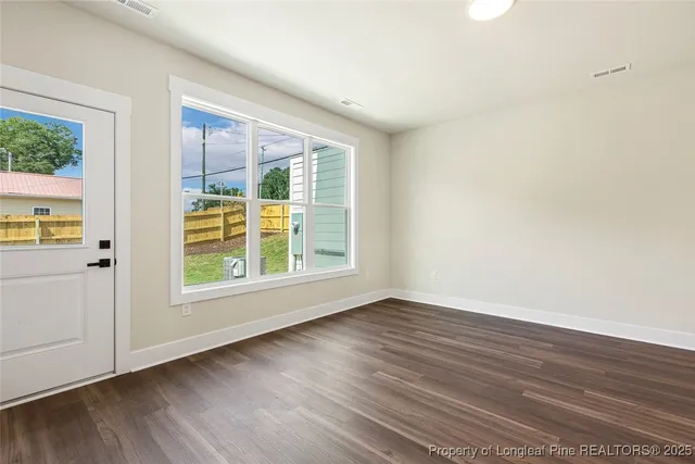 a view of an empty room with wooden floor and a window