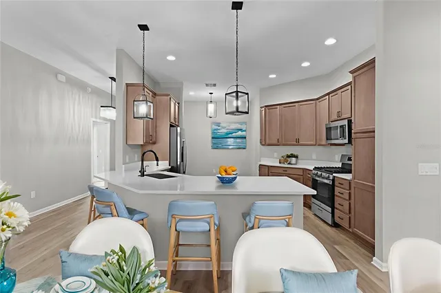 a kitchen with stainless steel appliances a refrigerator a sink a dining table and chairs with wooden floor