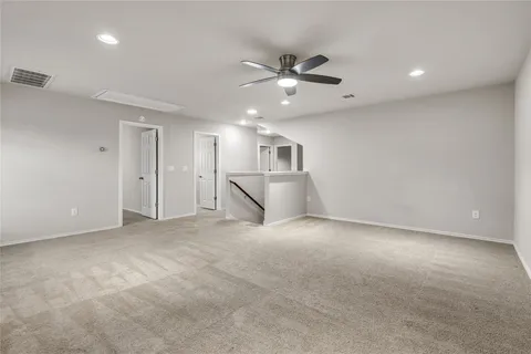 an empty room with a ceiling fan and kitchen view
