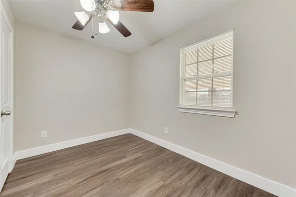 an empty room with wooden floor chandelier fan and windows