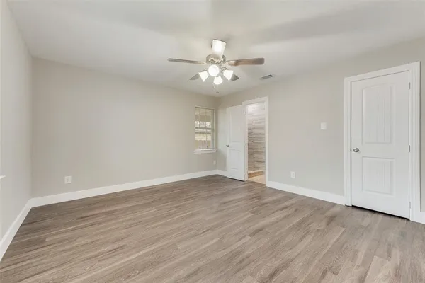 an empty room with wooden floor ceiling fan and window