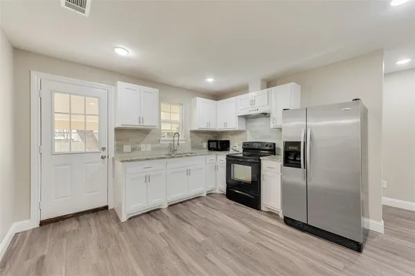 a kitchen with granite countertop a refrigerator oven a sink dishwasher and white cabinets with wooden floor