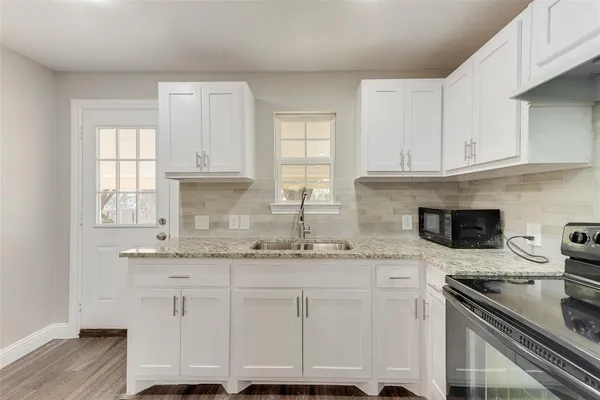 a kitchen with granite countertop a sink stainless steel appliances white cabinets and a window