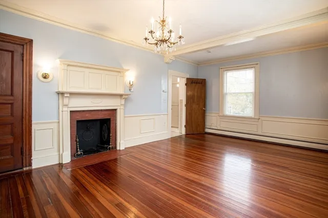 a view of an empty room with wooden floor fireplace and a window