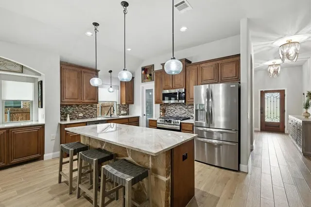 a kitchen with kitchen island a refrigerator a stove a kitchen island a dining table and chairs with wooden floor