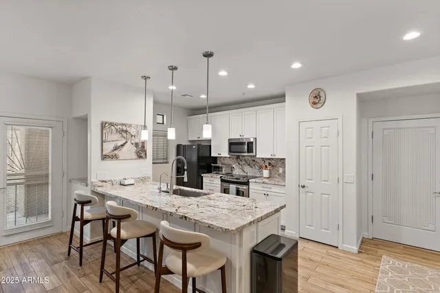 a kitchen with stainless steel appliances kitchen island granite countertop a dining table chairs and a refrigerator