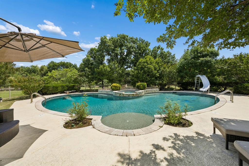 5808 Rathbone Drive Parker, TX 75002 - Photo 33 of 39 The area around is the pool is protected by a wrought iron fence. The decking is salted concrete and the pool coping is stone. Enjoy lounging on the tanning ledge or in the separate spa with waterfall. Fun abounds with the slide and diving board available!