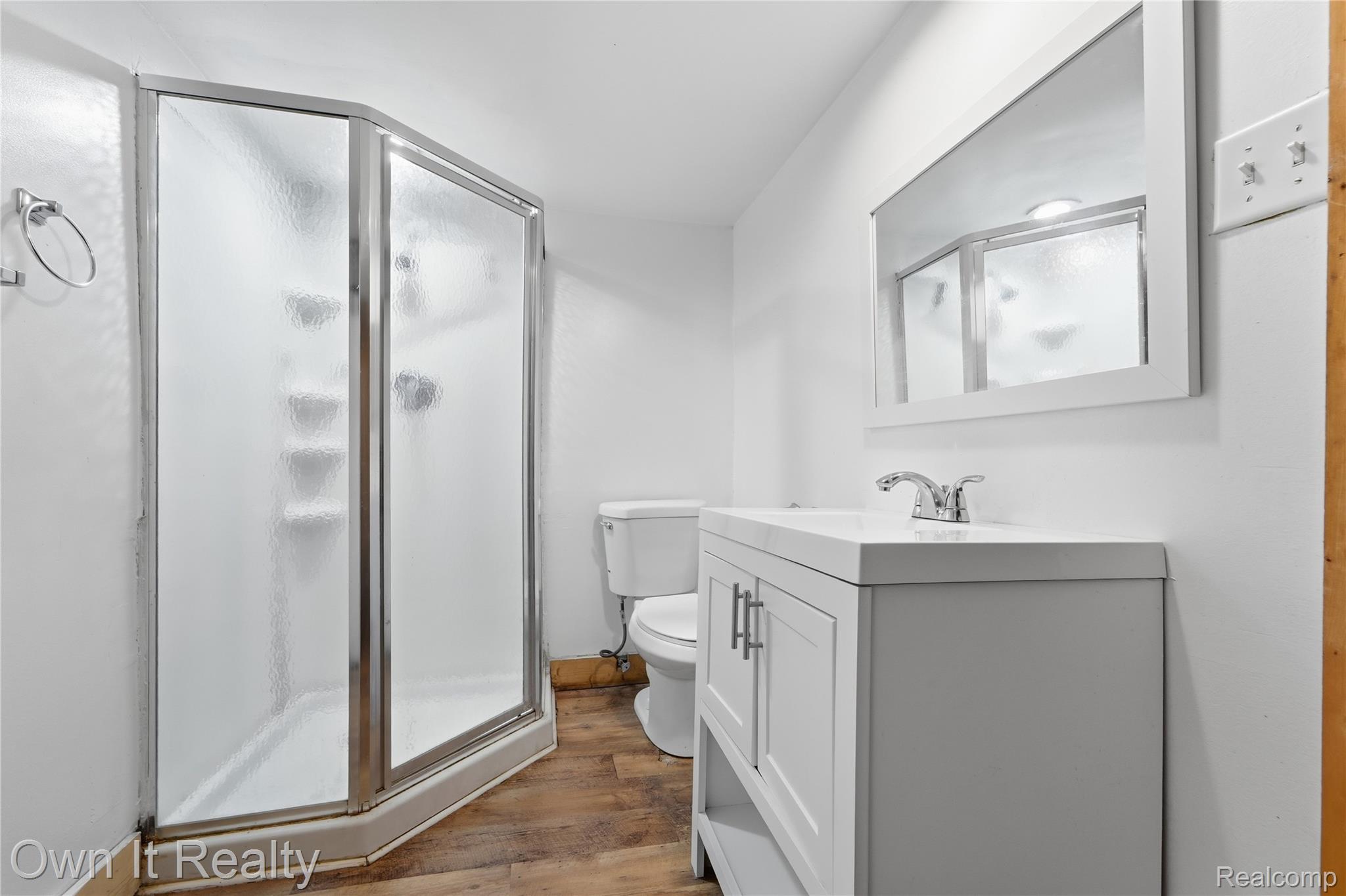 26772 Colgate Street Inkster, MI 48141 - Photo 21 of 25 Corner shower enclosure with frosted glass panels, white framed vanity mirror, white vanity with dual cabinet doors, chrome faucet, and wood-finish flooring
