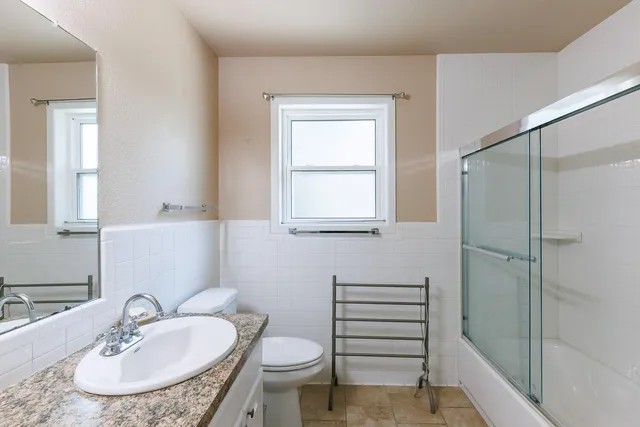 a bathroom with a granite countertop sink a toilet a mirror and shower