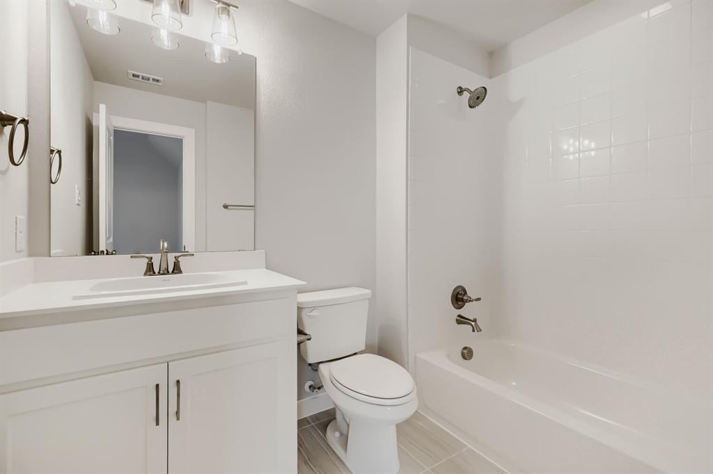 4407 Windy Point Road Oak Point, TX 75068 - Photo 23 of 27 Modern bathroom featuring a white vanity with integrated sink, brushed nickel fixtures, a full-sized mirror, and a tub-shower combination with white subway tile surround