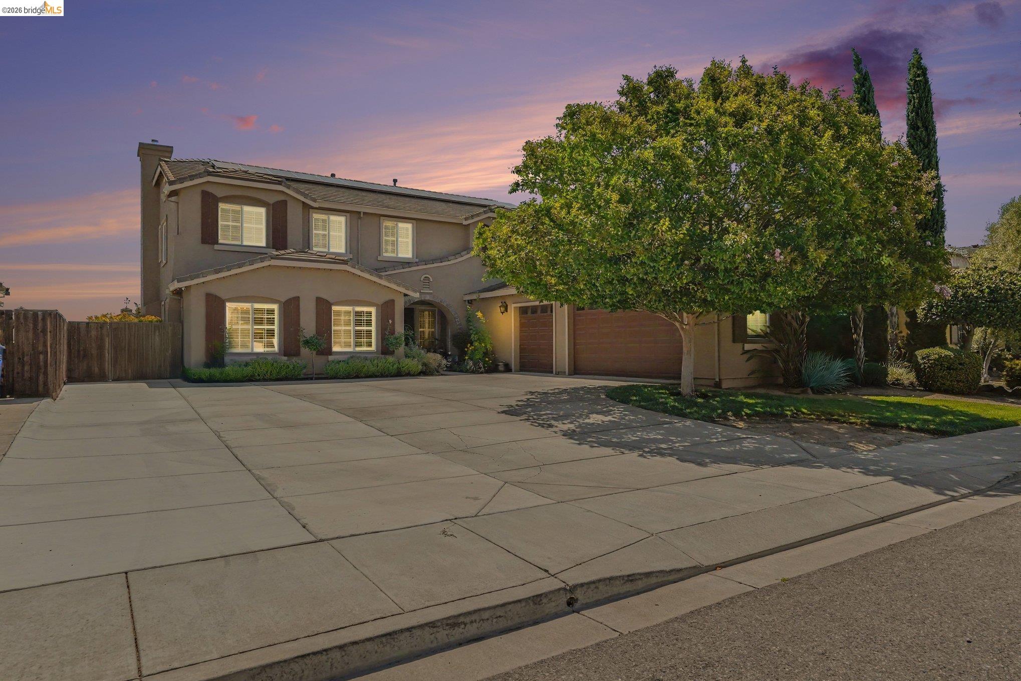 Stucco exterior residence with a large driveway, two-car garage, and mature tree landscaping