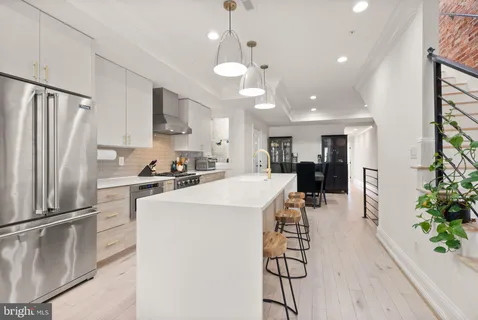 a kitchen view with stainless steel appliances a refrigerator a stove a sink a dining table and chairs with wooden floor