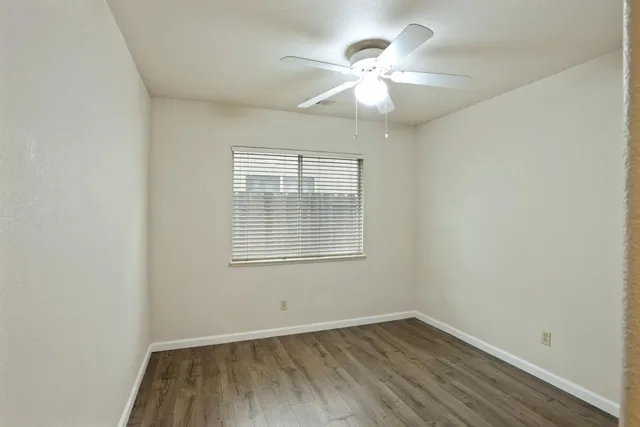 an empty room with wooden floor chandelier fan and windows