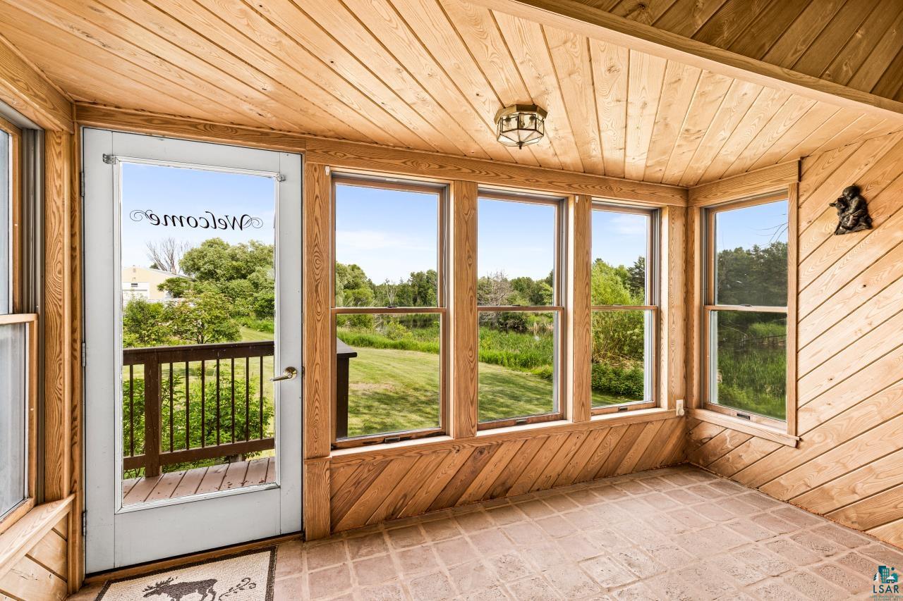 4800 Tower Road Moose Lake, MN 55767 - Photo 59 of 83 Wood-paneled room featuring multiple windows, a glass-paneled door opening to a deck with dark wood railing, and light-colored tile flooring