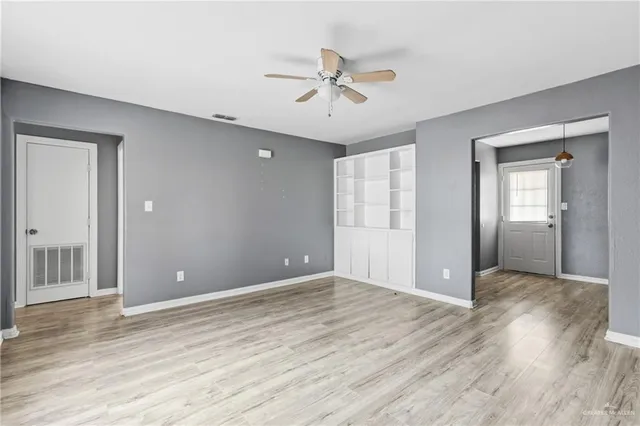 a view of an empty room with wooden floor and a ceiling fan