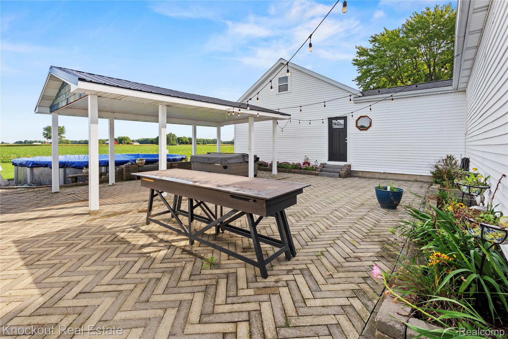 5750 Maple Road Frankenmuth, MI 48734 - Photo 48 of 60 Expansive paver patio with herringbone pattern, covered outdoor area, above-ground pool, and white siding exterior