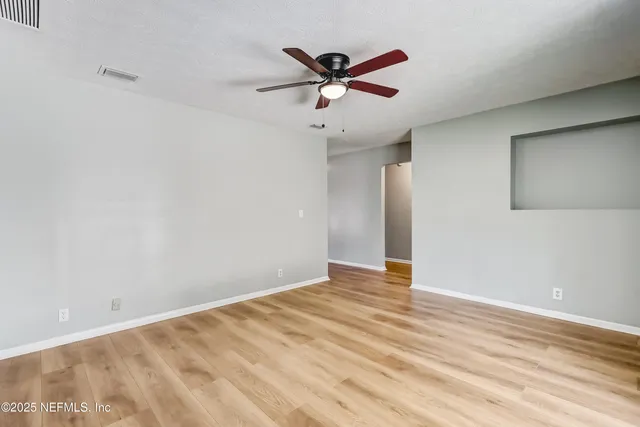 a view of an empty room with wooden floor and a ceiling fan