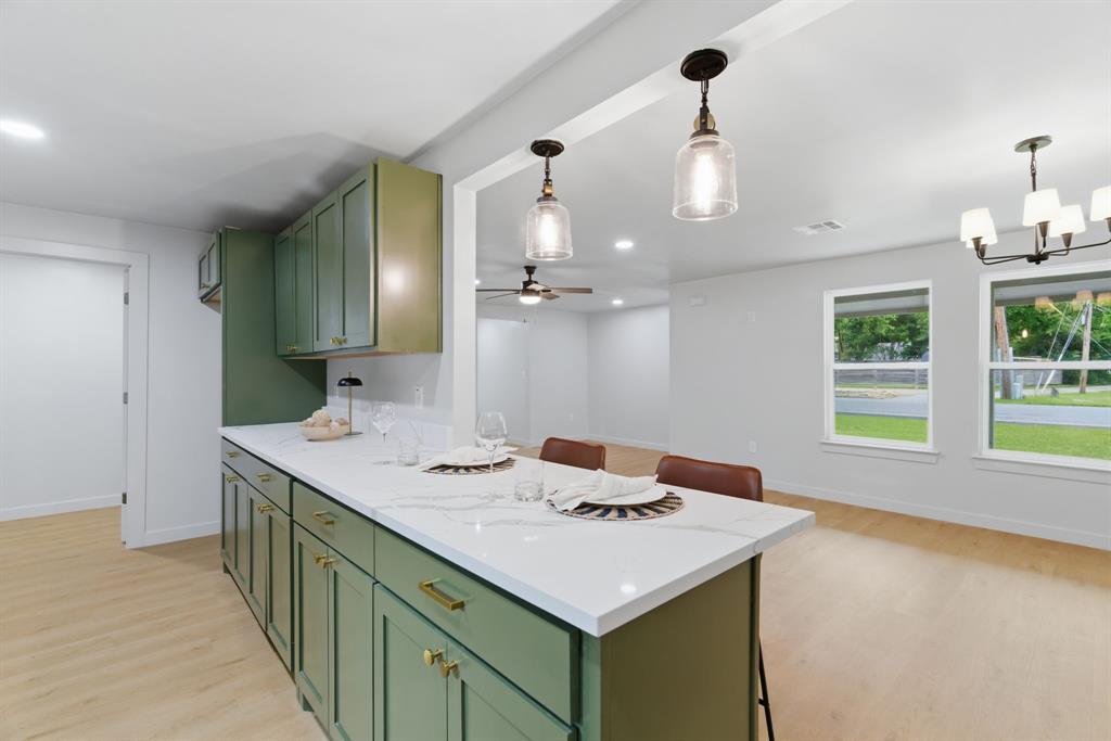 507 Country Club Road Cleburne, TX 76033 - Photo 15 of 39 Kitchen island featuring a white countertop, sage green cabinetry with gold hardware, and two pendant lights