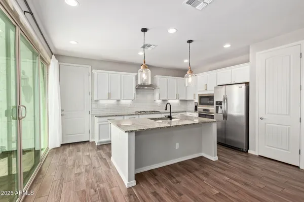 a kitchen with stainless steel appliances granite countertop a sink a stove a refrigerator and island with wooden floor